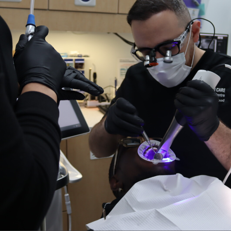 Dentist at Hamilton Care Dental Centre performing precision dental work with loupes and a curing light in Hamilton, Ontario