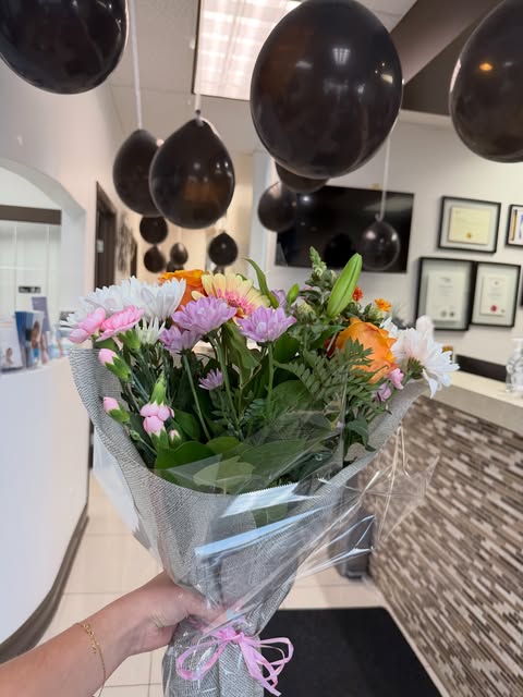 hand holding a colorful flower bouquet inside dental clinic with black celebration balloons hanging from ceiling