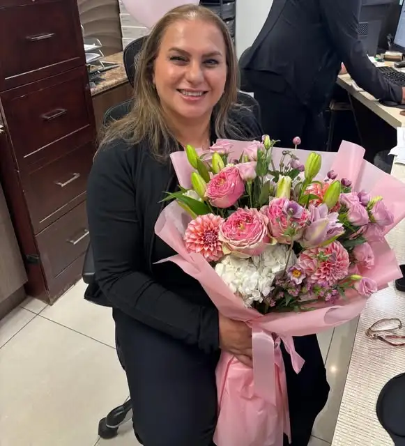 smiling staff member sitting in dental clinic holding a large pink flower bouquet