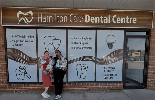 two dental staff members standing outside hamilton care dental centre holding gift baskets in front of window graphics